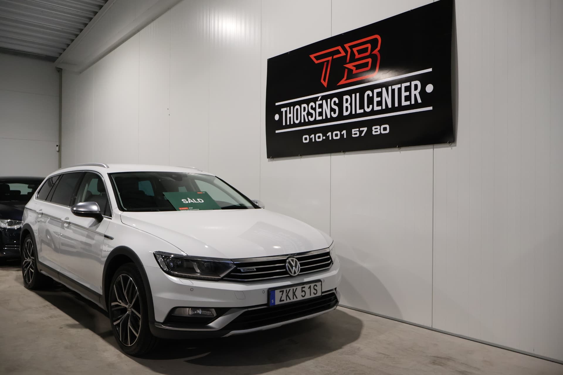 Vit Volkswagen Passat Alltrack framför Thorséns Bilcenters banderoll